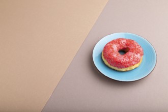 Pink Donut with sprinkles on blue ceramic plate on beige and gray pastel paper background, side