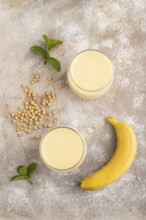 Organic non dairy banana and soy milk in glass on brown concrete background. Vegan healthy food