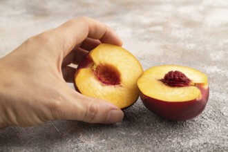 Peach Cut in half with hand on brown concrete background. Side view, copy space. healthy food,