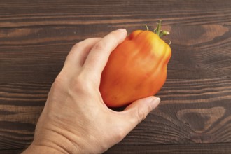 Red Heart Shape tomato with hand on brown wooden background. Top view, flat lay, close up. healthy
