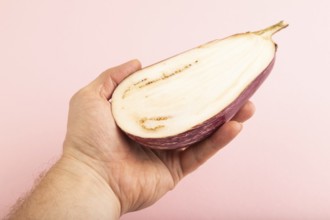 Hand holding sliced Purple eggplant with white stripes on pink pastel background. Side view, copy