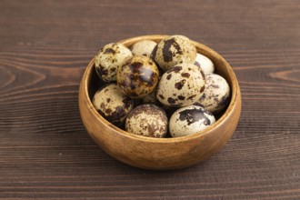 Pile of raw Quail eggs in bowl on a brown wooden background. side view, close up