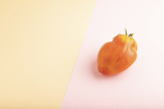 Red Heart Shape tomato on pink and orange pastel paper background. Side view, copy space. healthy