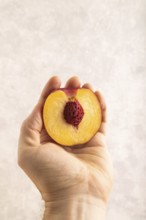 Peach Cut in half with hand on brown concrete background. Side view, copy space. healthy food,