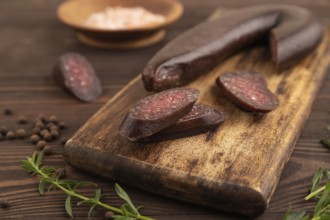 Sujuk sausage on wooden cutting board with pepper and herbs on brown wooden background. Side view,