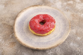 Pink Donut with sprinkles on blue ceramic plate on brown concrete background, side view, close up,