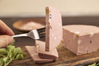Mortadella sausage with hand on wooden cutting board with pepper and herbs on brown wooden