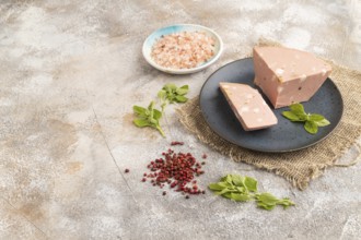 Mortadella sausage on plate with pepper and herbs on brown concrete background and linen textile.