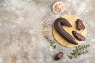 Sujuk sausage on wooden cutting board with pepper and herbs on brown concrete background. Top view,