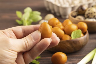 Pile of Smoked Quail eggs in bowl with hand on a brown wooden background. side view, close up,