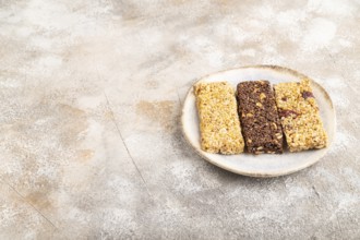 Granola bars with caramel, nuts, flakes in ceramic plate on brown concrete background. Side view,