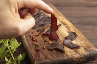 Armenian Basturma dried meat with hand on wooden cutting board with pepper and herbs on brown