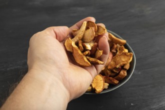 Dried Apples in ceramic bowl with hand on black wooden background. Side view, close up. healthy