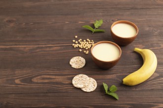 Organic non dairy banana and soy milk in clay cup on brown wooden background. Vegan healthy food