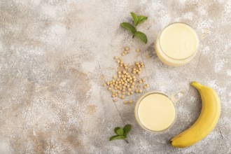 Organic non dairy banana and soy milk in glass on brown concrete background. Vegan healthy food