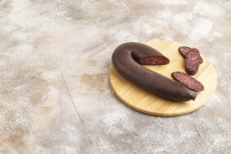 Sujuk sausage on wooden cutting board with pepper and herbs on brown concrete background. Side