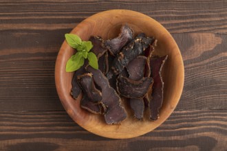 Armenian Basturma dried meat on wooden bowl with pepper and herbs on brown wooden background. Top
