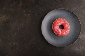 Pink Donut with sprinkles on blue ceramic plate on black concrete background, top view, flat lay,