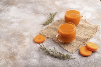 Two glasses with carrot juice, on brown concrete background and linen textile. Diet, healthy eating