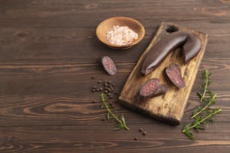 Sujuk sausage on wooden cutting board with pepper and herbs on brown wooden background. Side view,