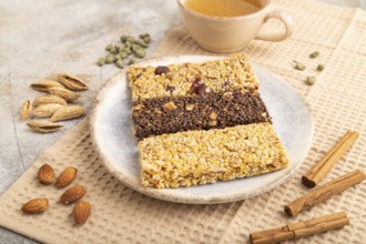 Granola bars with caramel, nuts, flakes in ceramic plate on brown concrete background, beige linen