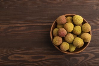 Ripe Lychee on clay bowl on brown wooden background, top view, flat lay, copy space, minimalism