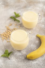 Organic non dairy banana and soy milk in glass on brown concrete background. Vegan healthy food