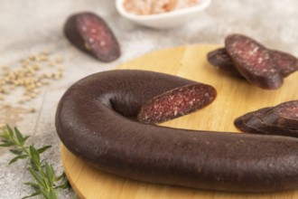 Sujuk sausage on wooden cutting board with pepper and herbs on brown concrete background. Side