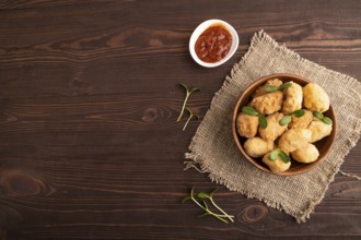 Fried crispy Chicken Nuggets with ketchup, microgreen on brown wooden background and linen textile.
