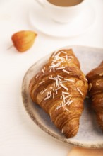 Croissant on blue plate on white wooden background and orange linen textile, cup of coffee, side