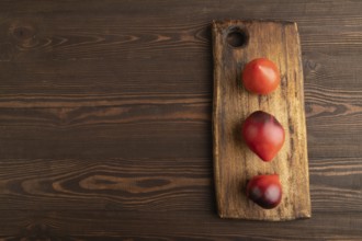 Yellow tomatoes on cutting board on brown wooden background. Top view, copy space, flat lay.