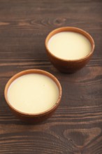 Organic non dairy banana and soy milk in clay cup on brown wooden background. Vegan healthy food