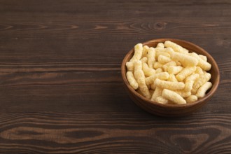 Corn flakes sticks with caramel in wooden bowl on brown wooden background. side view, copy space