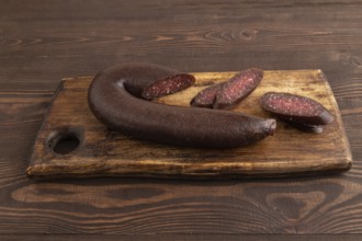 Sujuk sausage on wooden cutting board with pepper and herbs on brown wooden background. Side view,