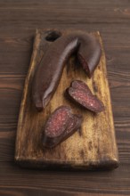 Sujuk sausage on wooden cutting board with pepper and herbs on brown wooden background. Side view,