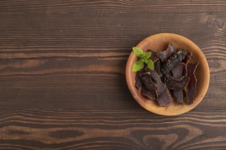 Armenian Basturma dried meat on wooden bowl with pepper and herbs on brown wooden background. Top