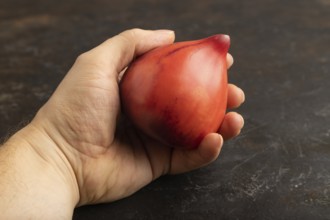 Red Heart shape tomatoes with hand on black concrete background. Side view, copy space. healthy