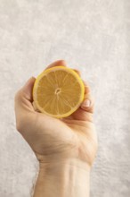 Yellow Lemon Cut in half with hand on gray concrete background. Side view, close up. healthy food,