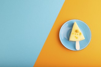 Yellow Cake pop with sprinkles on blue ceramic plate on blue and orange pastel paper background,