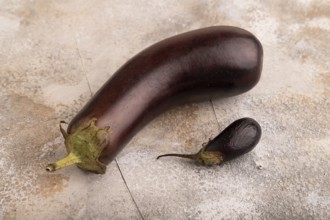 Two Eggplants big and small on brown concrete background, side view, close up, minimalism
