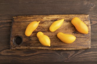Yellow tomatoes on cutting board on brown wooden background. Top view, copy space, flat lay.