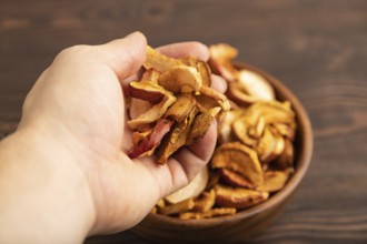 Dried Apples in wooden bowl with hand on brown wooden background. Side view, close up, healthy