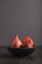 Red Heart shape tomatoes in blue bowl on black concrete background. Side view, copy space. healthy