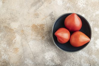 Red Heart shape tomatoes in blue bowl on brown concrete background. Top view, copy space, flat lay.