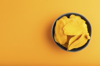 Dried Mango in blue ceramic bowl on orange pastel paper background. Top view, copy space, flat lay.