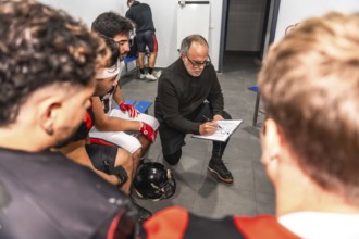 Football coach outlines game strategy on a clipboard while briefing his team in the locker room,