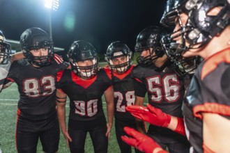 American football players huddling on a lit turf field at night, helmets on, focused on strategy
