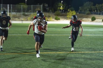 American football players competing on a lit field at night, a player carrying the ball and