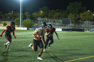 American football player vigorously running with the ball on a green field during a night game, two