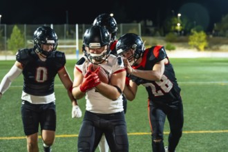 American football players in uniform and helmets engaging in a game on an illuminated sports field